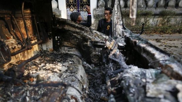 Anti-government protesters chat behind the remains of a burnt-out vehicle at the site of recent clashes with police near the Government house in Bangkok.