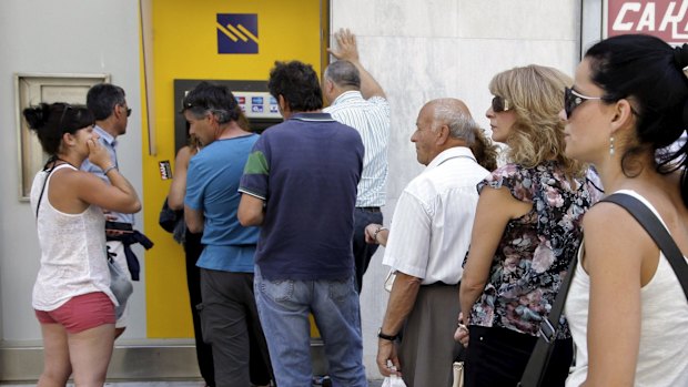 People line up to withdraw cash from an automated teller machine on the island of Crete.