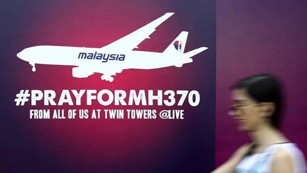A woman walks past a board reading "Pray for MH370" for passengers aboard a missing Malaysia Airlines plane.