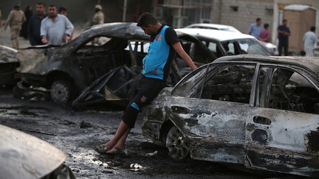 Iraqi men gather at the scene of one of the two car bombs that exploded in Baghdad's Habibiyah area on Monday.