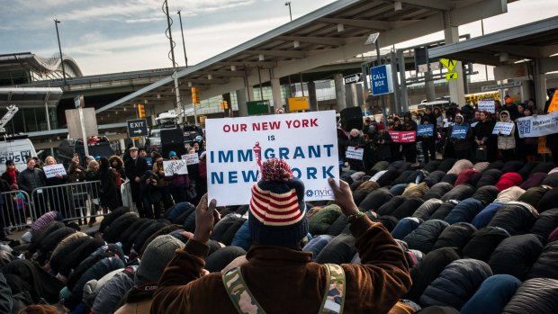 A group of Muslim men pray while supporters hold up signs during an interfaith prayer and rally against the ban at John F. Kennedy Airport.