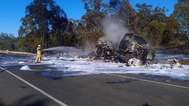 A firefighter hoses down a truck destroyed by fire on the Bruce Highway.