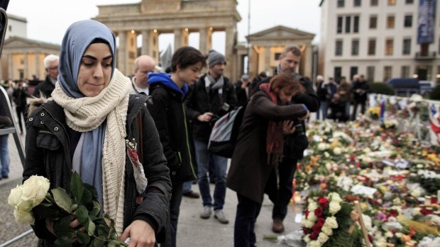 A young Muslim woman holds white roses outside the French Embassy among candles, messages and flowers left by mourners commemorating the victims of the terrorist attacks in Paris.