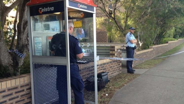 A police officer dusting a public phone for fingerprints at River Terrace, Kangaroo Point, where a 27-year-old woman was stabbed.