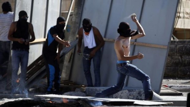A masked Palestinian protester throws stones  during clashes in East Jerusalem.