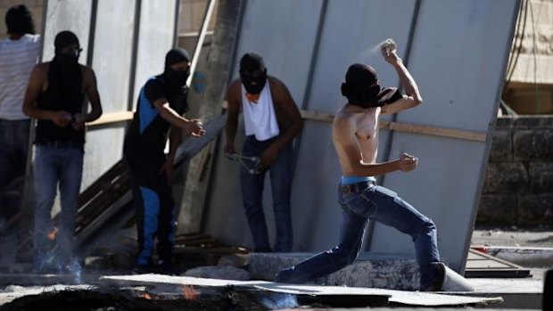 A masked Palestinian protester throws stones  during clashes in East Jerusalem.