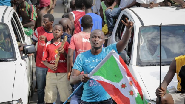 A demonstrator holds the Burundi national flag and makes the victory sign as he and others celebrate the military coup d'etat, in the capital Bujumbura, Burundi.
