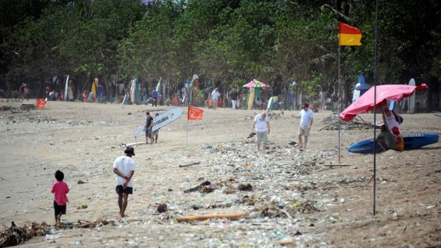 Foreign tourists and locals walk along the popular Kuta Beach covered with debris and rubbish.