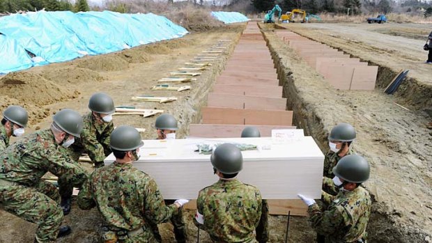 Mass grave ...  soldiers bury another victim of the earthquake and tsunami as the confirmed death toll rose above 9000 with more than 12,000 listed as missing.