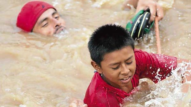 A man attempts to rescue a boy who tried to cross the overflowing Huiza River in El Salvador.