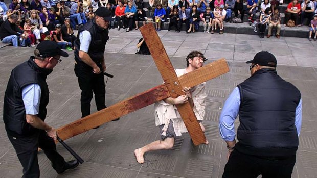 Three men playing security officers taunt another man playing Jesus Christ during a modern interpretation of the crucifixion  played out on Good Friday by members of Wesley Mission in Sydney.