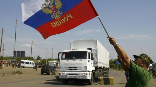 A local resident holds a Russian national flag as the trucks cross the Ukrainian border.
