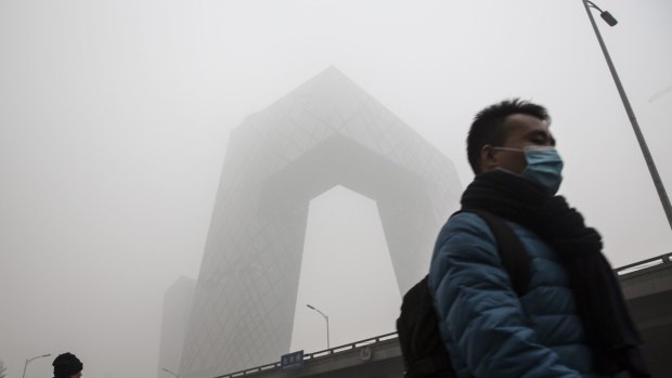 A pedestrian wearing a face mask walks past China Central Television headquarters building, which is shrouded in haze. 