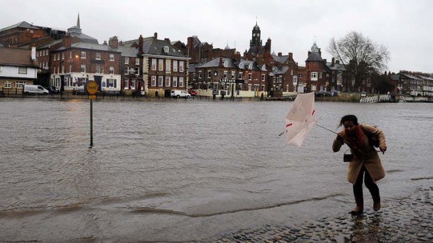 A woman struggles with her umbrella as rising water levels from the River Ouse bring floodwater into riverside roads in York, England.