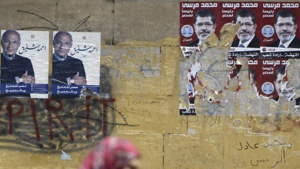 A woman walks past election campaign posters of presidential candidates Mohamed Mursi and Ahmed Shafiq.
