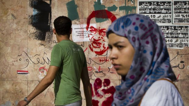 Egyptians walk past graffiti caricaturing Egypt's former President Hosni Mubarak.