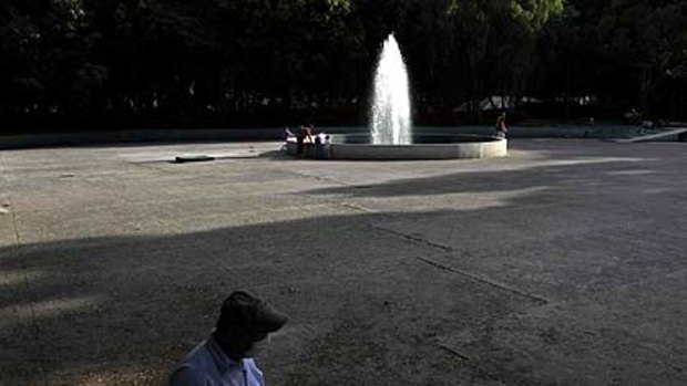 A man with a protective face mask passes a nearly empty park as a few children play in the fountain in Mexico City.