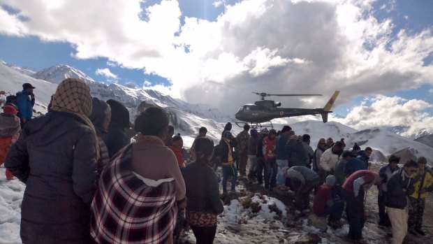 A Nepalese Army helicopter takes off as survivors of a snowstorm in Manang District on the Annapurna Circuit hiking trail look on.