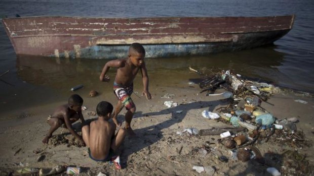 Boys play next to an abandoned boat, on the garbage-littered shore of Guanabara Bay.