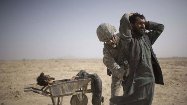 A US soldier in Kandahar province searches a man following a missile strike on Taliban bomb planters.
