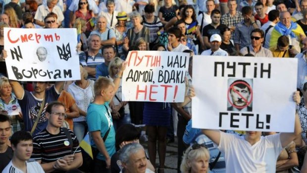 People hold placards (LtoR) reading "Putin get out!", "Putin go home, there is no vodka!" and "Death for enemies!", during a rally in the centre of the southern Ukrainian city of Mariupol.