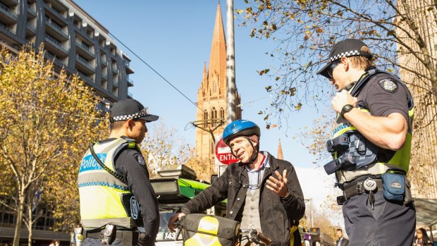 Police talk to a cyclist about riding through red lights at the intersection of Swanston and Collins streets.