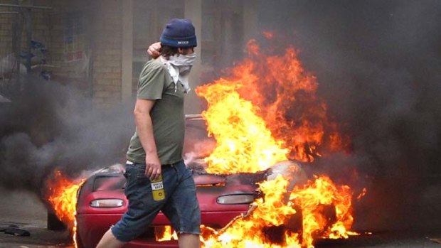 Riots ... a masked man walks past a burning car in Hackney.