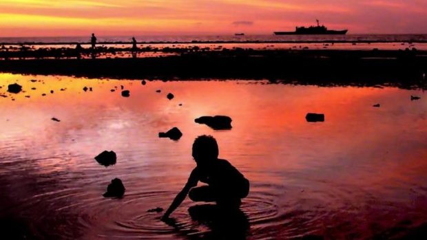 Boundary: A child collects shells as an Australian navy ship patrols along the shore in Dili, East Timor.