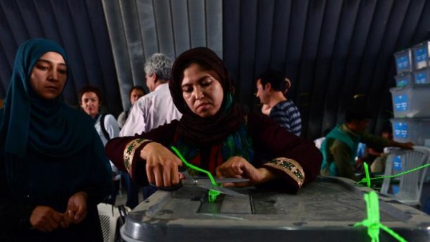 An Afghan election commission worker cuts open seals to a  ballot box.