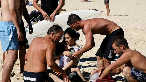 The mother of the rescued toddler comforts her daughter as lifeguards revive her.