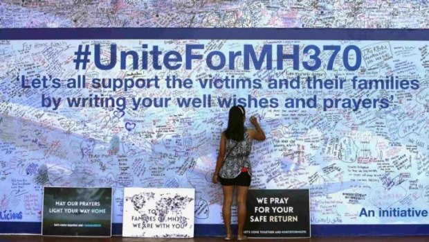 A woman writes on a board  in Kuala Lumpur dedicated to those onboard MH370.