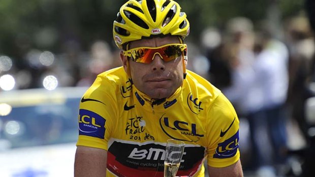 Cadel Evans holds a glass of champagne as he rides in the last stage of 2011 Tour de France.