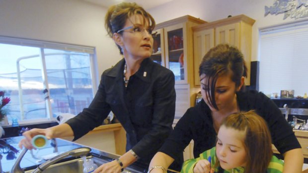 Back home again: Palin mixes baby formula as her daughters Willow and Piper decorate a cake.