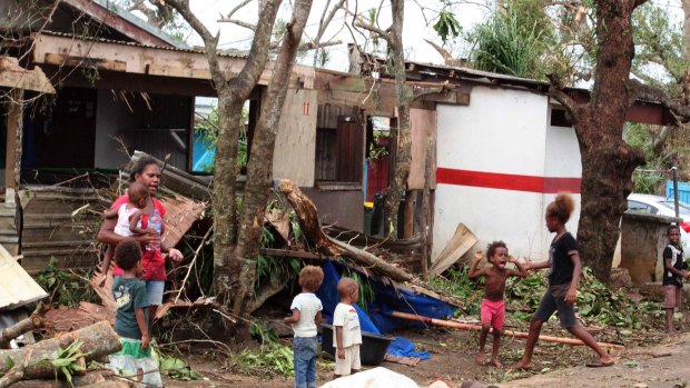 A woman carrying a baby stands with children outside homes damaged by Cyclone Pam in Port Vila.