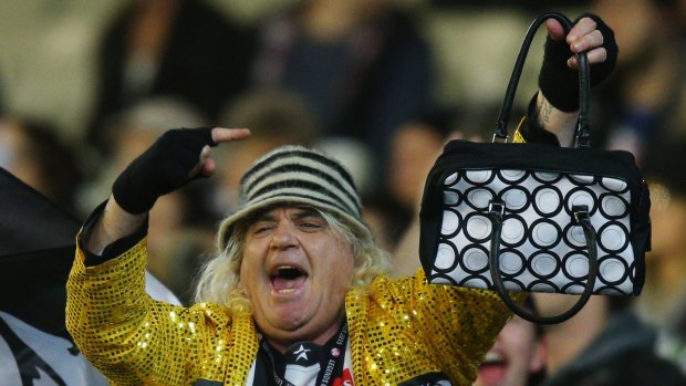 Magpies cheer squad leader Joffa Corfe adds insult to injury, holding up a handbag to Cats fans.