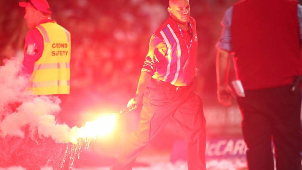 A security guard handles a flare during the round three A-League match between Sydney FC and the Western Sydney Wanderers at Allianz Stadium