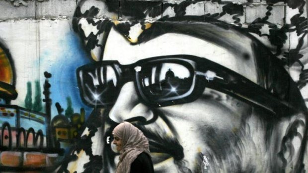 A woman walks past a mural of former Palestinian leader Yasser Arafat.