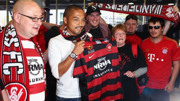 Shinji Ono holds a Western Sydney Wanderers playing shirt as he poses with supporters after his arrival at Sydney International Airport.
