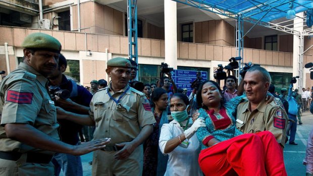 A policeman carries away a woman wounded in the New Delhi High Court blast while, below, armed officers stand guard.