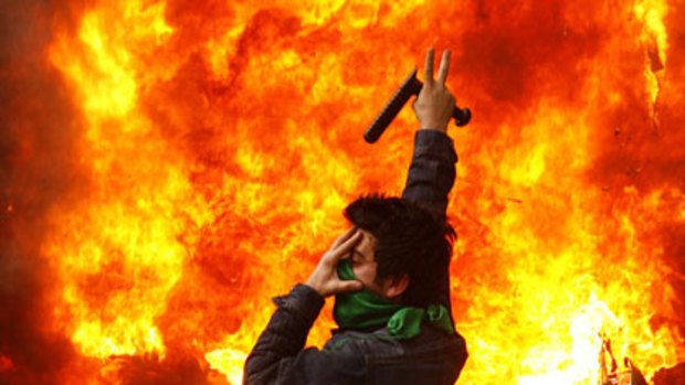 An opposition supporter gestures next to a burning police motorcycle set on fire during the clashes.