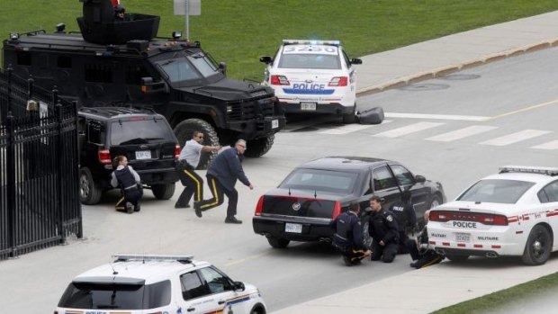 Police officers take cover near Parliament Hill following the shooting.