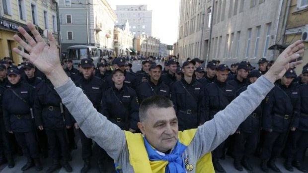 A man with a Ukrainian flag on his shoulders stands near a riot police line standing guard during an anti-war rally in Moscow, September 21, 2014.