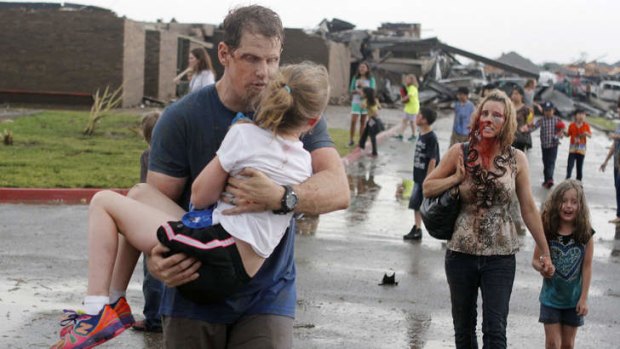 Escape from the ruins: Steve Cobb carries daughter Jordan while wife Ledonna walks with a pupil. The couple saved both children from the tornado-ravaged school.