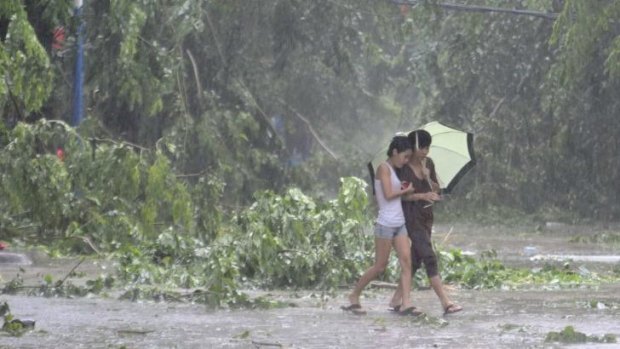 Residents hold an umbrella as they walk on a street in front of fallen tree branches during heavy rainfall under the influence of Typhoon Kalmaegi in Qionghai, Hainan province.