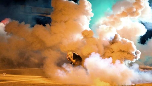 A protester takes shelter from a smoke bomb.
