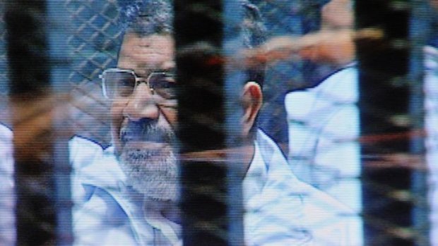Mohamed Mursi in a soundproof barred glass cage as seen on a monitor outside the courtroom.