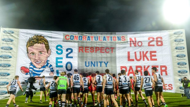 Sydney and Geelong players break through the banner together.