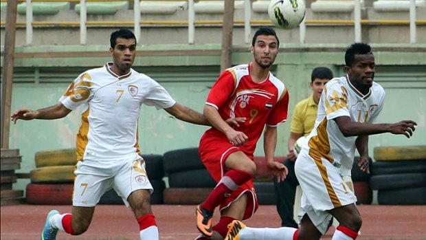 Syria's Ahmad Al-Doni (C) fights for the ball with Mohammed Al-Seyabi (L) and Saad Al-Mukhaini (R) of Oman.