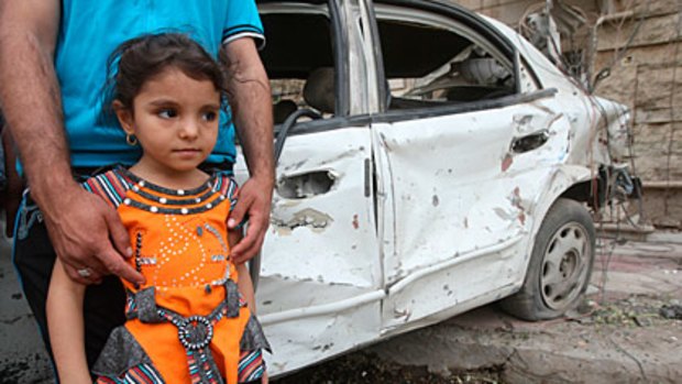 A Christian Iraqi child stands by her father’s destroyed car.