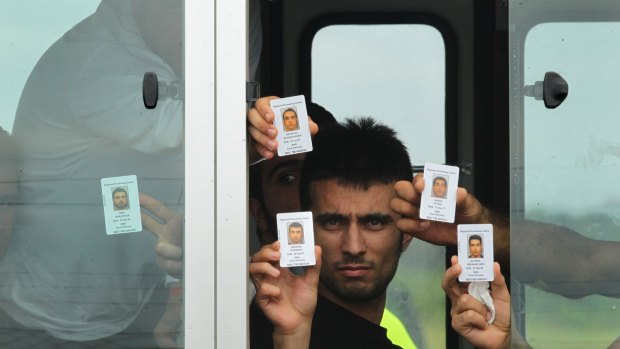 Pezhma Ghorbani 26 from Iran (centre) along with his fellow asylum seekers holds his ID card at the window of the bus after arriving on the second plane carrying asylum seekers to  Manus Island in Papua New Guinea. August 2, 2013. 